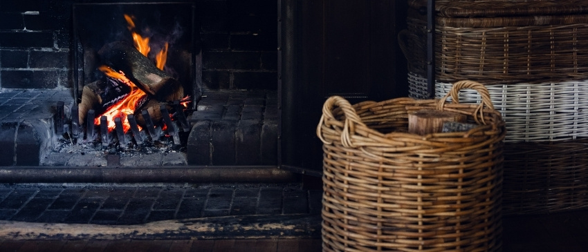 Open fireplace beside woven firewood baskets at Links House in Bowral